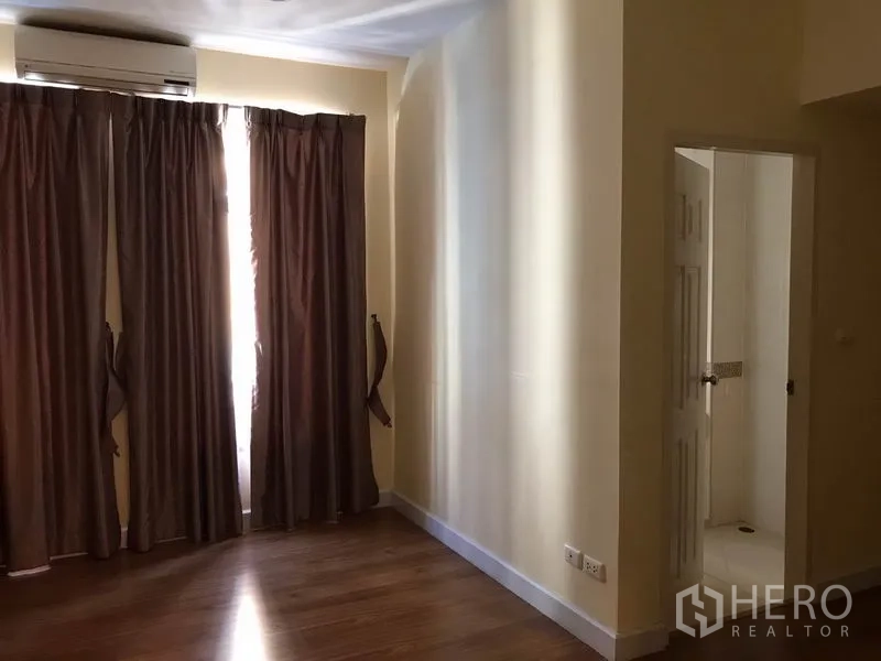 Townhouse for rent in Wang Thonglang, Bangkok - Bedroom with wood floors, brown curtains, wall air-conditioning and door to an en-suite bathroom.