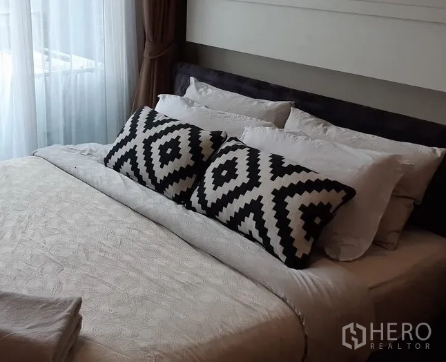 คอนโด ให้เช่าในKhlong Toei, Bangkok - ห้องนอนพร้อมเตียงใหญ่ หมอนลายขาวดำ และแสงจากระเบียงผ่านผ้าม่าน