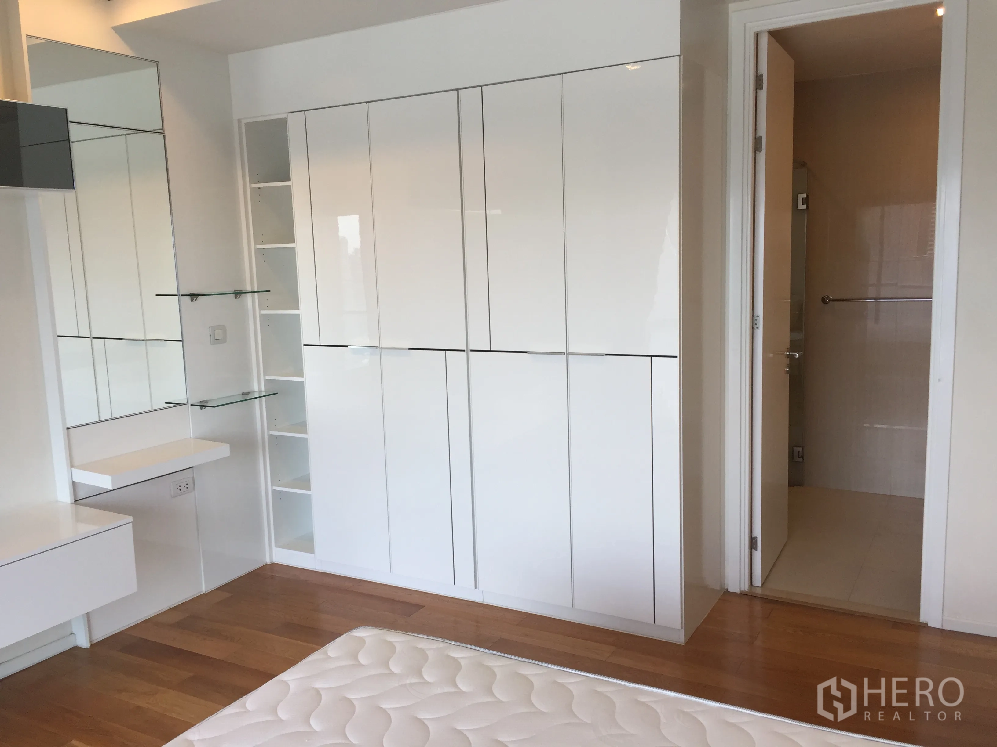 公寓 出租在Ratchathewi, Bangkok - 卧室一角设高光衣柜、玻璃搁板与通往浴室的门。