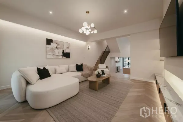 联排别墅 出租在Watthana, Bangkok - 明亮客厅，超大沙发、楼梯与嵌灯。