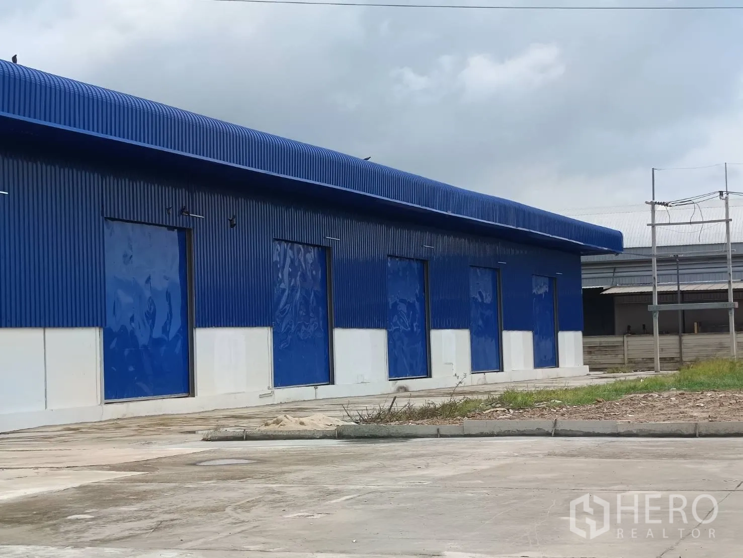 Warehouse for rent in Bang Len, Nakhon Pathom - Side elevation of steel warehouse with multiple blue roller shutter loading doors.