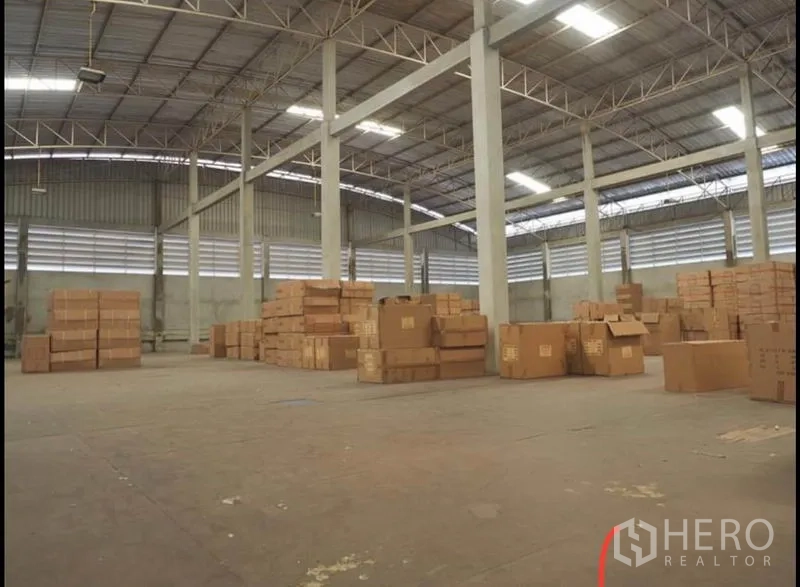 Warehouse for rent in Nakhon Pathom - Spacious storage hall with concrete columns, metal trusses, and multiple stacks of cardboard boxes.