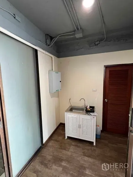 办公空间 出租或出售在Suan Luang, Bangkok - 小型茶水间，带水槽和储物柜，旁为推拉玻璃隔断。