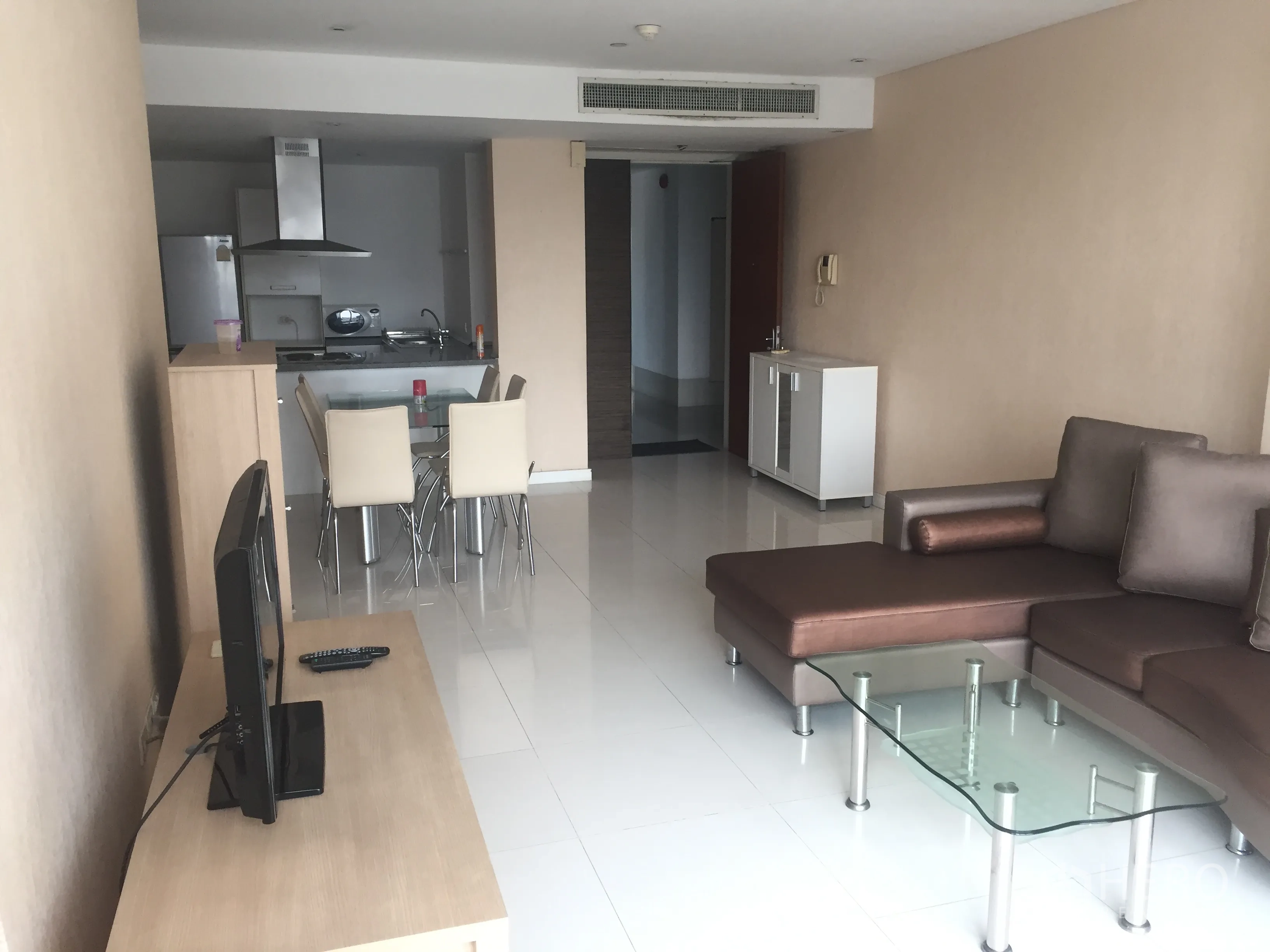 Condominium for rent or sale in Watthana, Bangkok - Open-plan living and dining area with sectional sofa, glass coffee table, TV stand, and modern kitchen in an Ekkamai condo.
