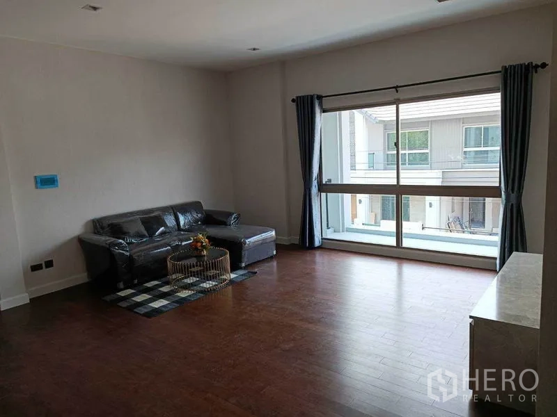 Detached House for rent in Bueng Kum, Bangkok - Bright upstairs living area with wood flooring, L-shaped sofa, and floor-to-ceiling window.