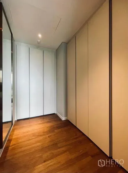 Condominium for rent in Pathum Wan, Bangkok - Walk-in closet corridor with full-height wardrobes and warm wood flooring.