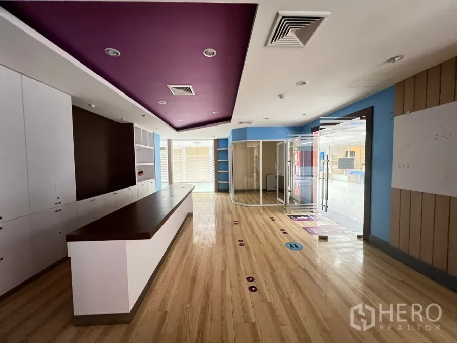 零售空间 出租 - 店铺内部配有长型内置前台、木地板、紫色吊顶与玻璃门入口。