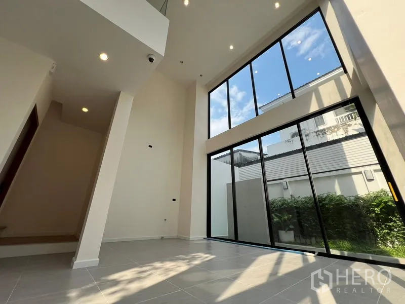 สำนักงานที่บ้าน ขายในPhra Khanong, Bangkok - ห้องนั่งเล่นเพดานสูง กระจกเต็มผนังรับวิวสวนและแสงธรรมชาติ.