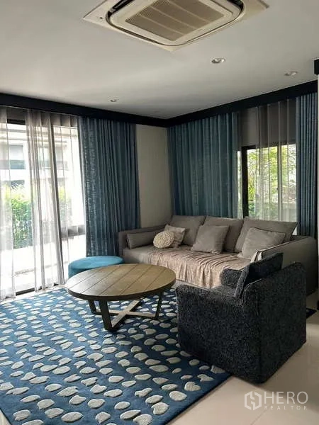 Detached House for rent in Bang Kapi, Bangkok - Cozy living room with sofa, armchair, blue patterned rug and floor‑to‑ceiling windows.