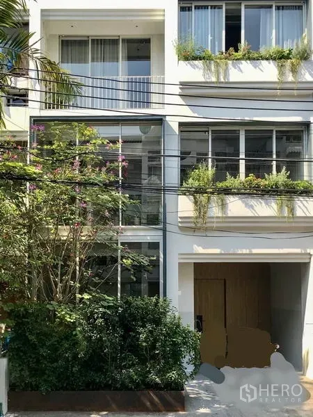 Townhouse for rent in Khlong Toei, Bangkok - Modern three-storey white townhouse facade with large windows and greenery planters.