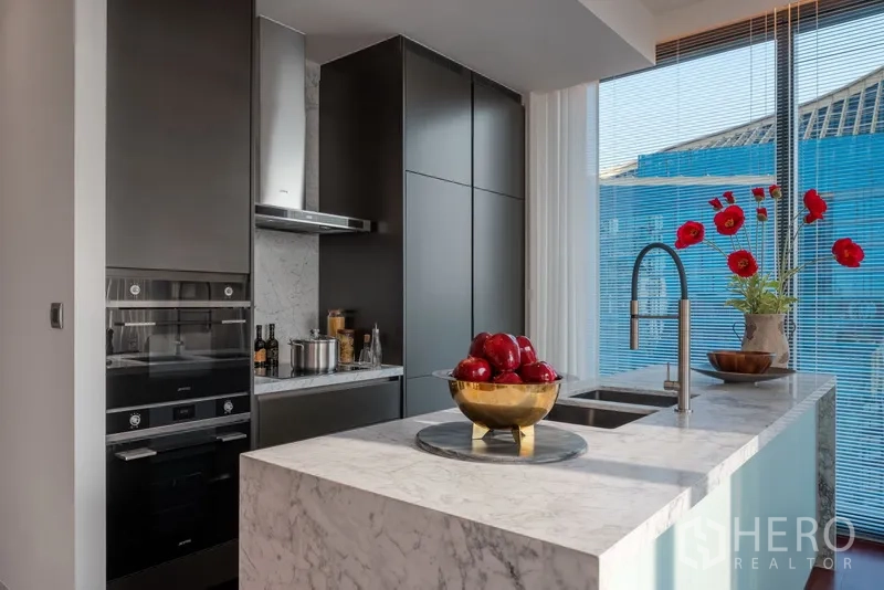 Condominium for sale in Watthana, Bangkok - Modern kitchen with dark cabinetry, built‑in ovens and a marble peninsula with sink.