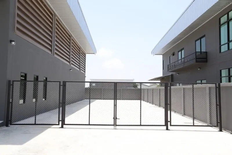 Factory for rent or sale in Bang Bo, Samut Prakan - Secure fenced yard between buildings with a chain-link sliding gate.