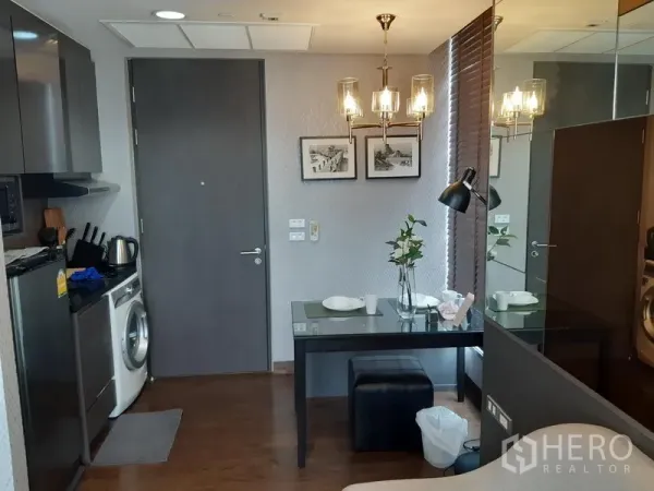 คอนโด ให้เช่าในKhlong Toei, Bangkok - ครัวบิวท์อินพร้อมตู้เย็น ไมโครเวฟ เครื่องซักผ้า และโต๊ะรับประทานอาหาร 2 ที่นั่ง ใต้โคมไฟแชนเดอเลียร์และผนังกระจก