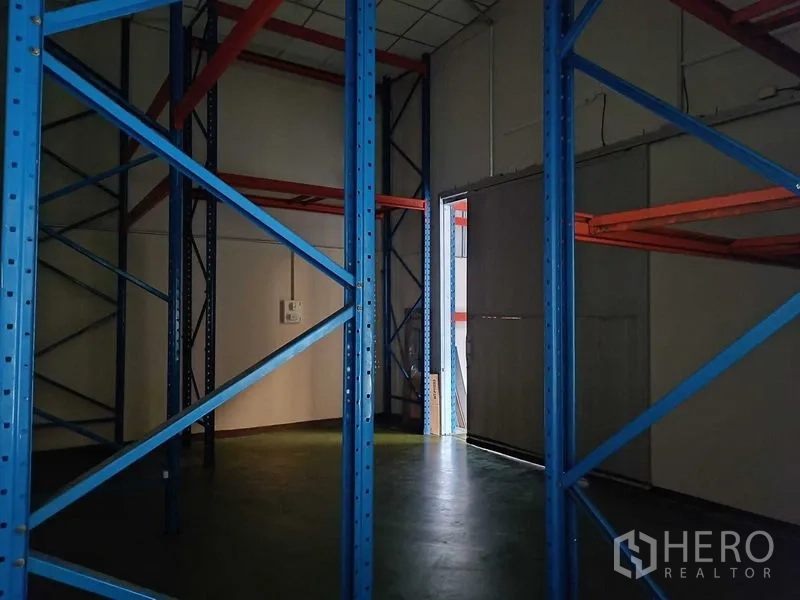 Warehouse for rent in Suan Luang, Bangkok - Close-up between steel racking frames next to a doorway with light.