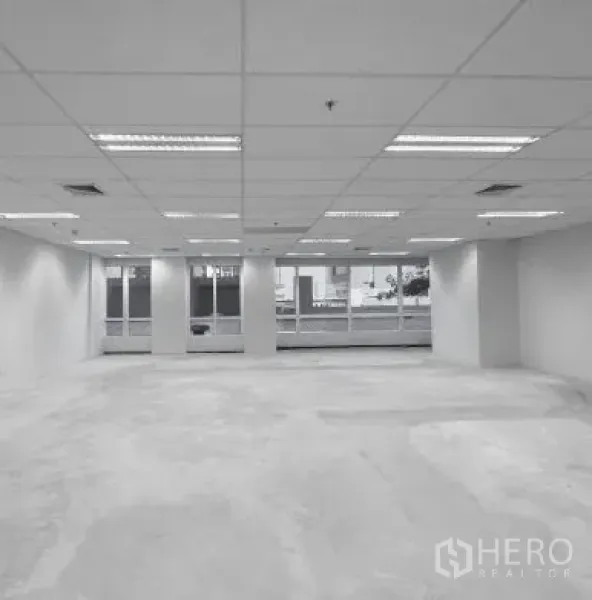 Office Space for rent - Open office area with columns, grid ceiling lighting and windows facing skyline.