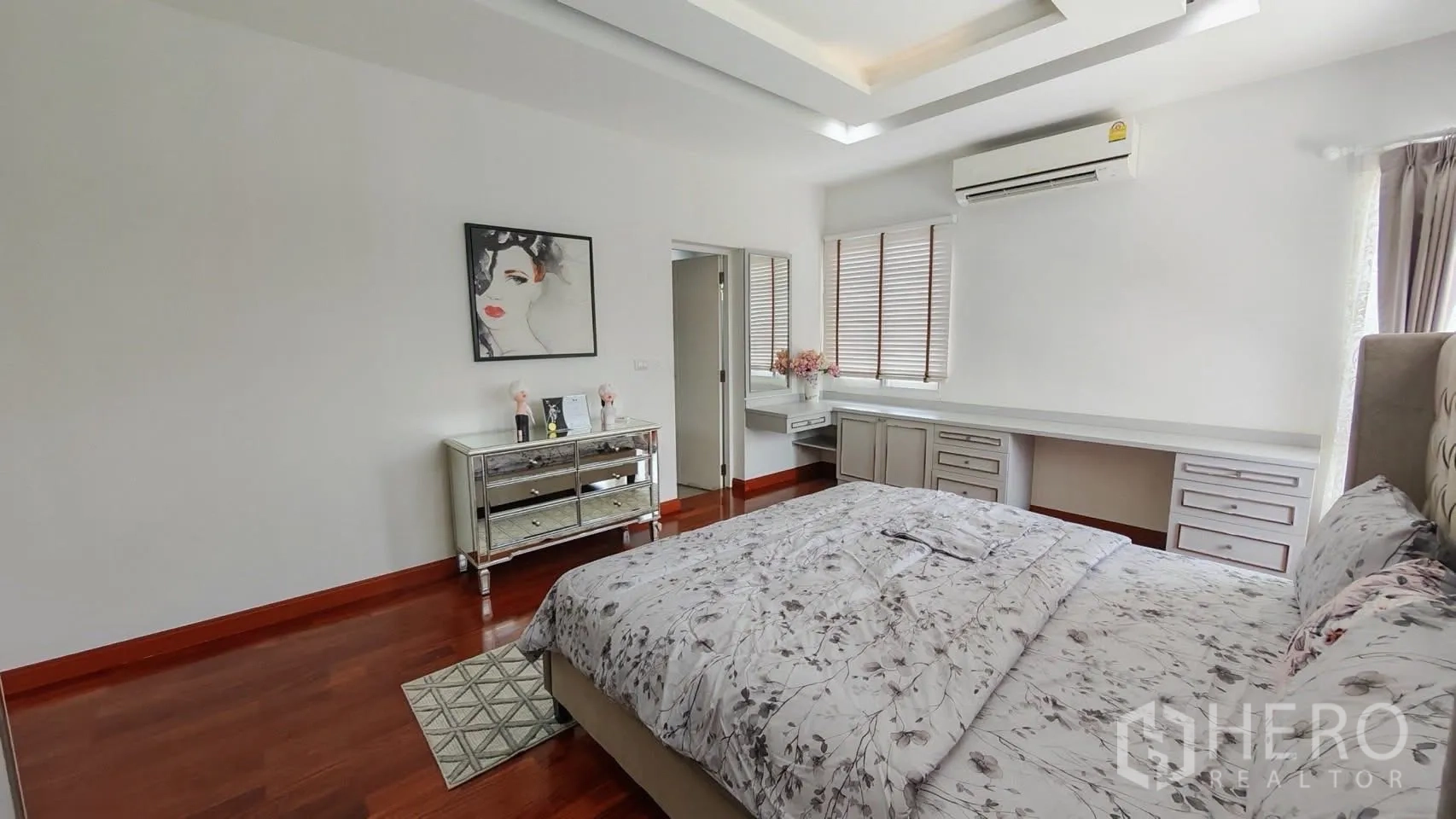Detached House for rent or sale in Bang Phli, Samut Prakan - Bedroom with king bed, mirrored dresser, and a long built-in vanity beneath window blinds.