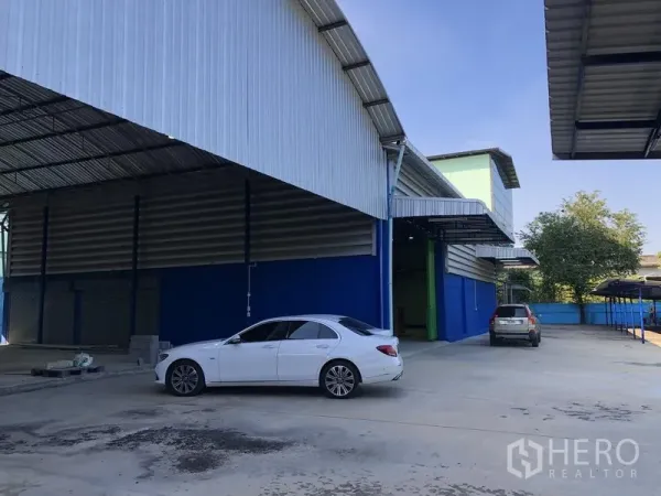 Warehouse for rent in Sai Mai, Bangkok - Large warehouse bays with metal roofs and a wide concrete yard for car and truck access.