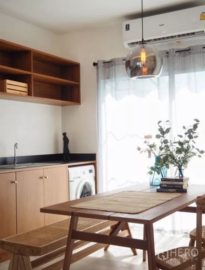 Townhouse for rent in Bang Phli, Samut Prakan - Open-plan dining area with wooden table, pendant light, kitchenette, built-in cabinets and washing machine nook.
