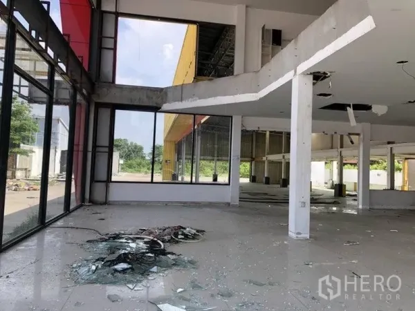 Retail Space for rent in Khlong Luang, Pathum Thani - Double-height showroom interior with floor-to-ceiling windows, columns and debris, ready for renovation.