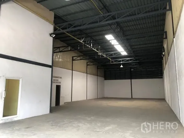 Warehouse for rent in Pak Kret, Nonthaburi - Open warehouse bay with high ceiling, skylights, and smooth concrete flooring.