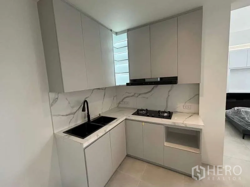 Townhouse for rent or sale in Don Mueang, Bangkok - Compact L-shaped kitchen with marble-look backsplash, twin sinks and gas hob.