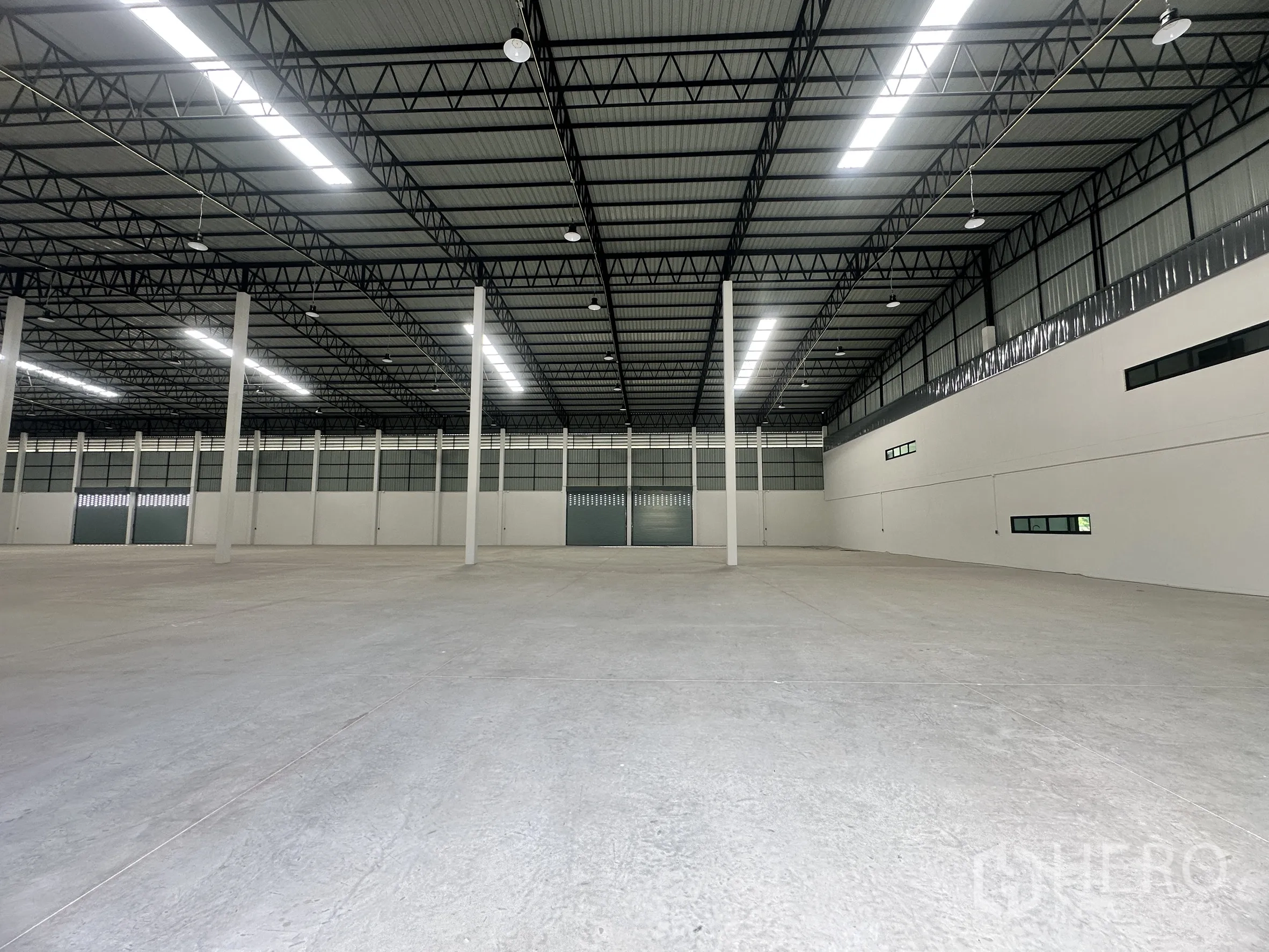 Factory for rent or sale in Bang Len, Nakhon Pathom - Open production space with tall columns, overhead lights, and multiple large loading doors.