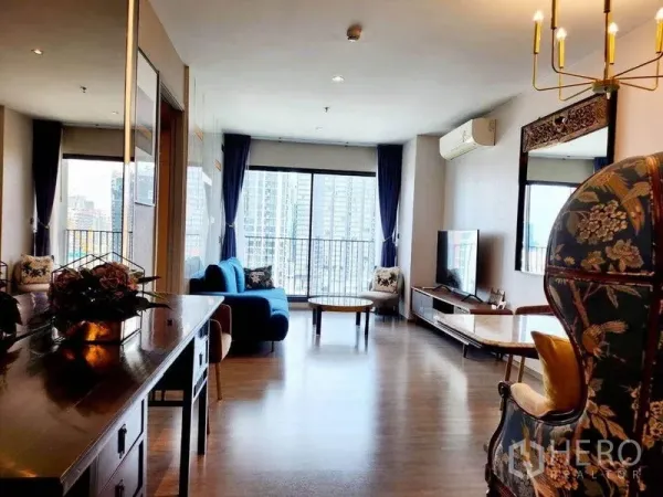 คอนโด ให้เช่าในWatthana, Bangkok - ห้องนั่งเล่นสว่างพื้นไม้ โซฟาสีฟ้า ชุดทีวี และหน้าต่างเต็มบานเปิดสู่ระเบียงวิวตึกสูงกรุงเทพฯ