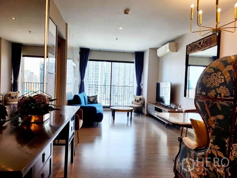 คอนโด ให้เช่าในWatthana, Bangkok - ห้องนั่งเล่นสว่างพื้นไม้ โซฟาสีฟ้า ชุดทีวี และหน้าต่างเต็มบานเปิดสู่ระเบียงวิวตึกสูงกรุงเทพฯ