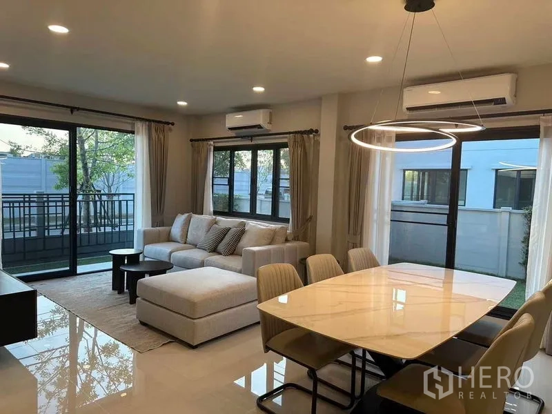 Detached House for rent in Bang Phli, Samut Prakan - Dining area with ring chandelier beside a cozy sofa set and sliding doors to the garden terrace.