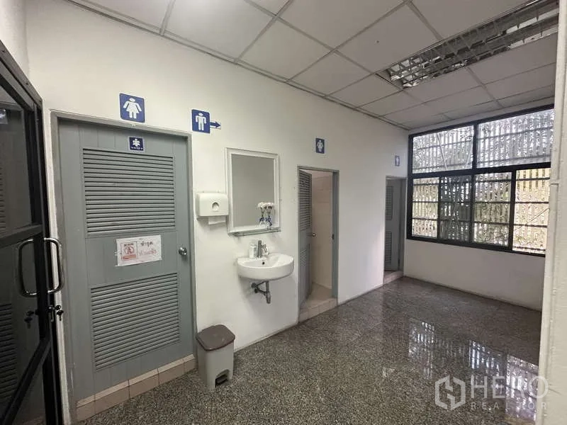 Warehouse for rent in Khlong Sam Wa, Bangkok - Restroom lobby with male and female toilet doors, sink and natural light.