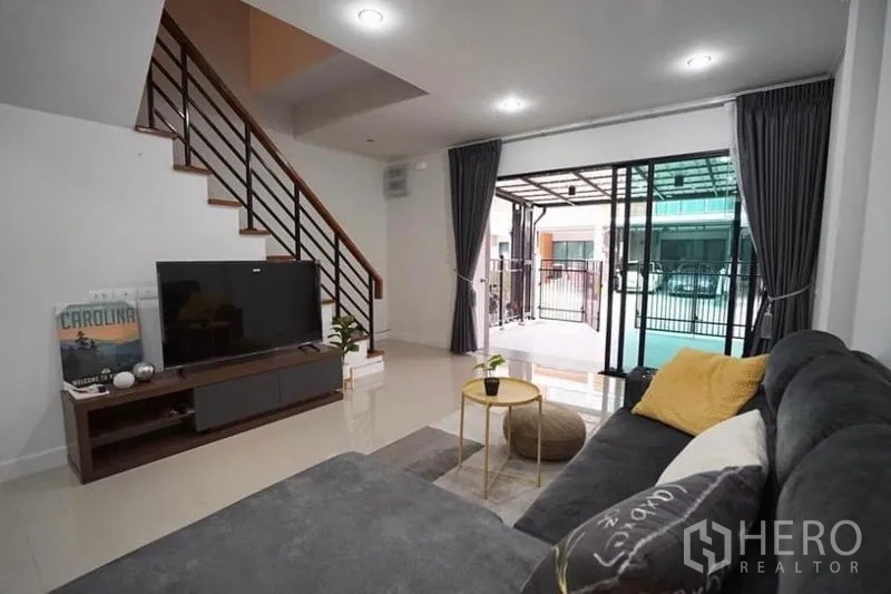Townhouse for rent in Bang Kapi, Bangkok - Living area facing sliding doors to a covered carport with dark curtains and recessed ceiling lights.