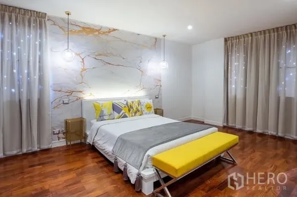คอนโด ให้เช่าในPathum Wan, Bangkok - ห้องนอนใหญ่ ผนังลายหินอ่อน โคมไฟห้อย ม้านั่งปลายเตียงสีเหลือง และหน้าต่างบานใหญ่พร้อมม่านโปร่ง