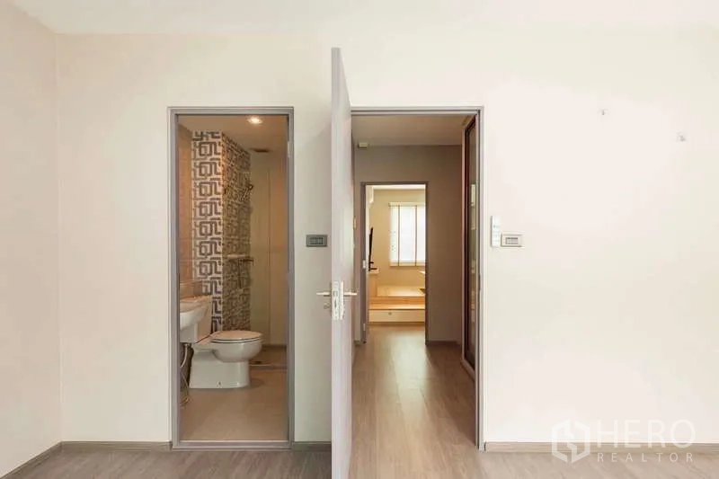 联排别墅 出租或出售在Lat Phrao, Bangkok - 卧室门与套内卫浴，木地板走廊通向地台客厅。