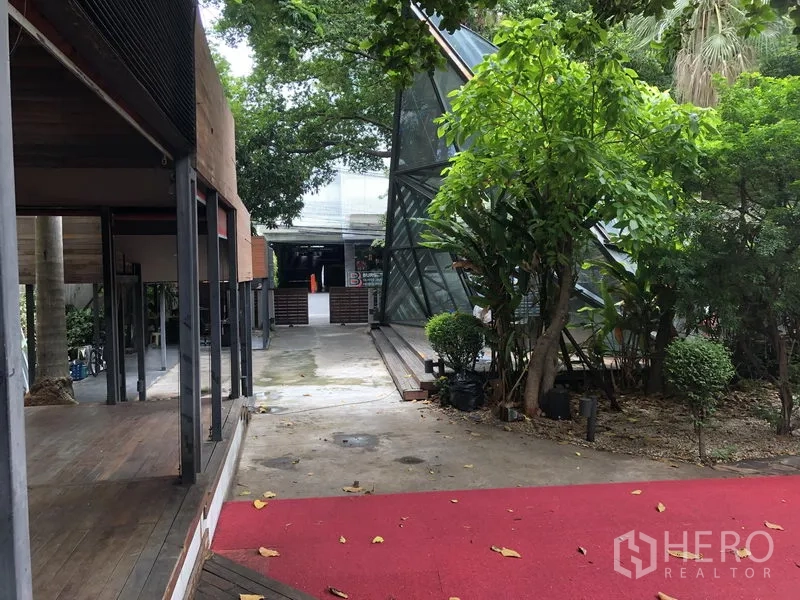 零售空间 出租在Bang Khae, Bangkok - 花园步道铺设红毯，三角形玻璃结构与成荫树木。