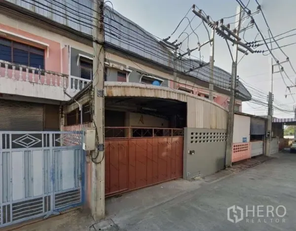 货栈 出租在Mueang Samut Sakhon, Samut Sakhon - 带遮雨装卸区与棕色金属门，临宁静的混凝土小路及上方电线。