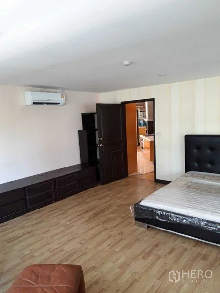 Condominium for sale - Large bedroom with air conditioner, wood floors, and dark wood cabinetry.