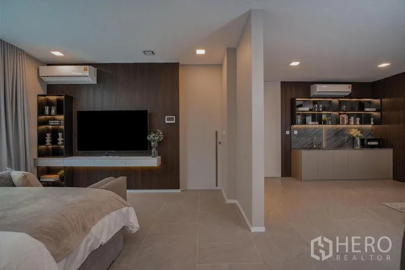 บ้าน ให้เช่า - โซนห้องนอนพร้อมมุมนั่งเล่น ผนังทีวี และแพนทรีบิลท์อิน พร้อมเครื่องปรับอากาศ.