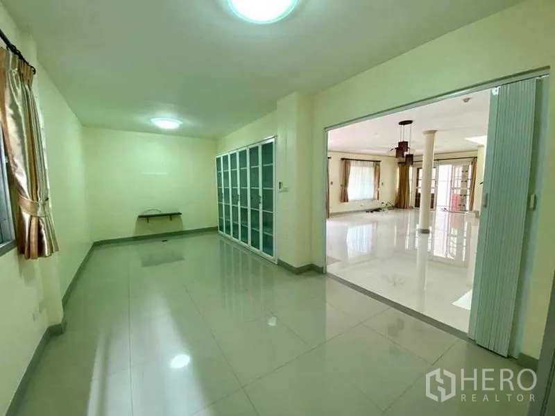 Detached House for sale in Phasi Charoen, Bangkok - Multi‑purpose room with glossy floor, built‑in glass cabinets, and sliding partition opening to a spacious living area.