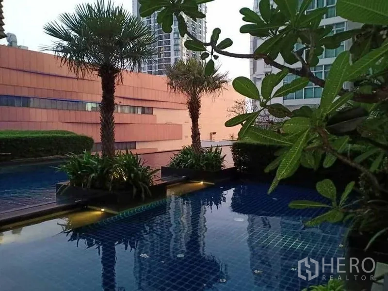 คอนโด ให้เช่าในKhlong Luang, Pathum Thani - สระว่ายน้ำคอนโดพร้อมต้นปาล์มและสวนสีเขียวบนดาดฟ้า