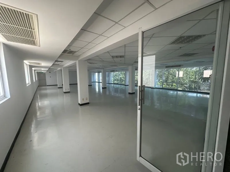 Office Space for rent in Phaya Thai, Bangkok - Hallway leading into a wide office area through a glass door with natural light and greenery outside.
