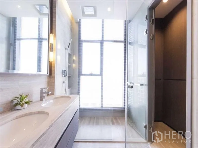 Condominium for rent in Bang Rak, Bangkok - Modern bathroom with double vanity, glass-enclosed shower and a large window bringing in natural light.