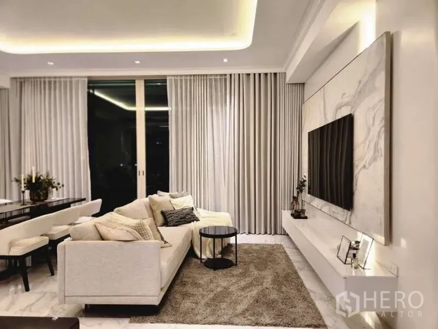 Condominium for sale in Watthana, Bangkok - Elegant living room with marble TV wall, area rug and sliding balcony doors.