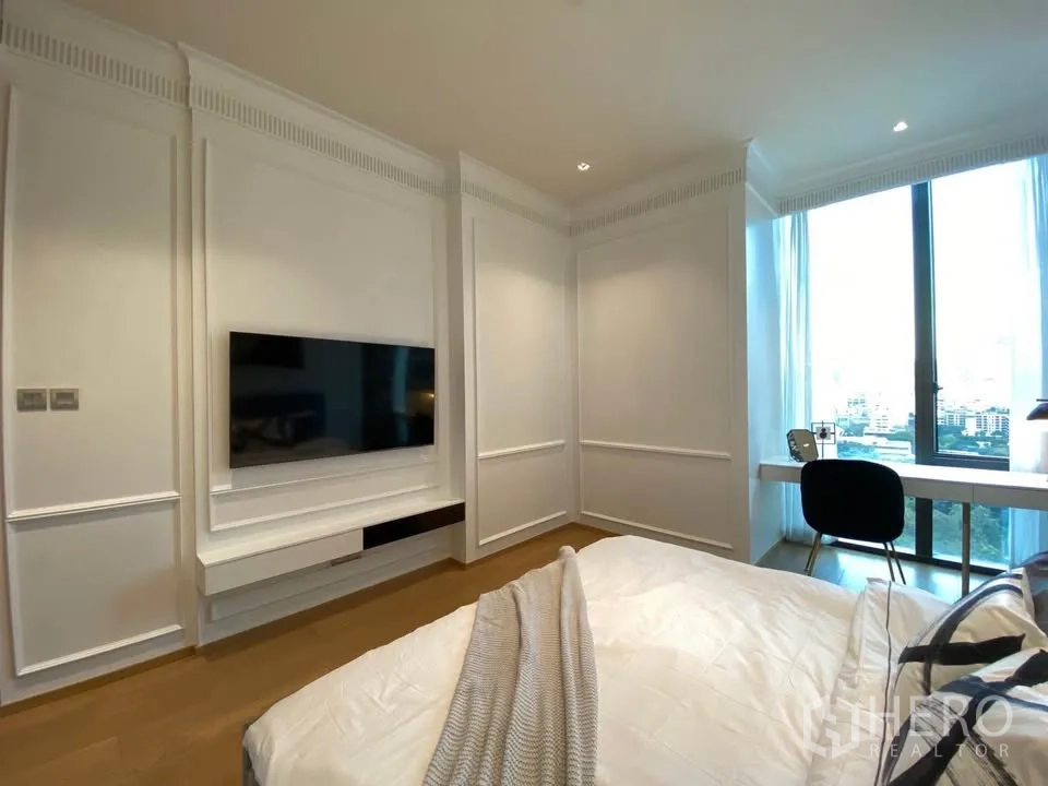 Condominium for rent in Pathum Wan, Bangkok - Bedroom facing a wall-mounted TV and long window with sheer curtains and city outlook.