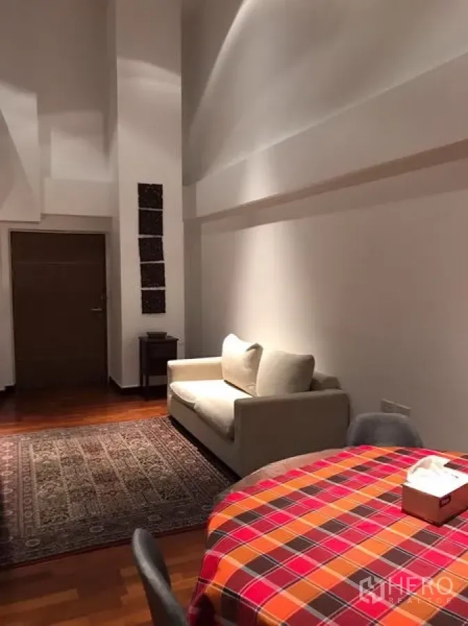 คอนโด ให้เช่าในWatthana, Bangkok - มุมห้องนั่งเล่น โซฟาสีครีม พรมลาย และเพดานสูง ในคอนโดย่านทองหล่อ