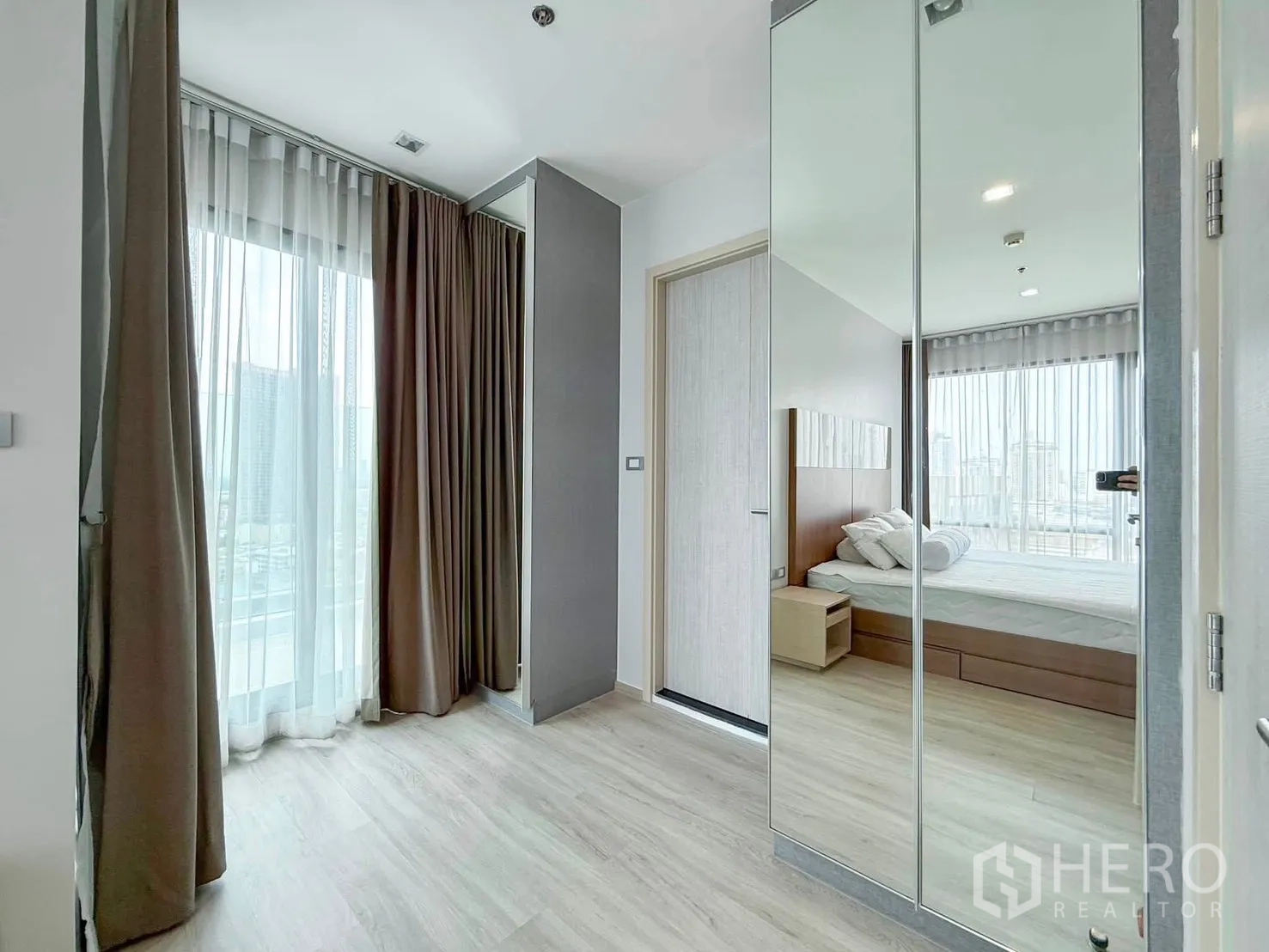 Condominium for rent in Khlong Toei, Bangkok - Hallway with mirrored closet leading into a bedroom with city outlook.
