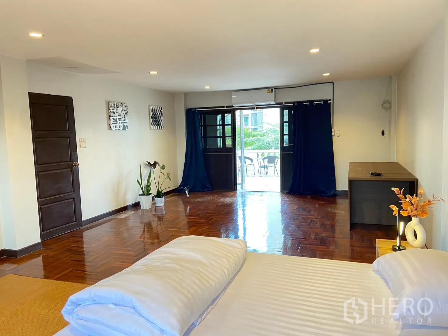 Home Office for rent in Watthana, Bangkok - Spacious bedroom with parquet floor, bed, balcony doors with blue curtains and an air conditioner.