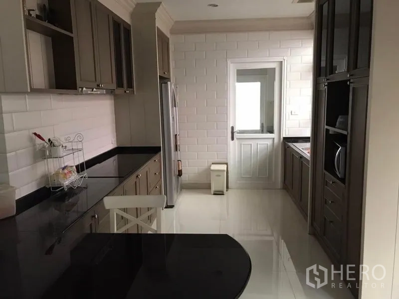 独立式住宅 出租在Bang Khen, Bangkok - 走廊式厨房，白色地铁砖墙面、内置柜体与通往杂物区的门。