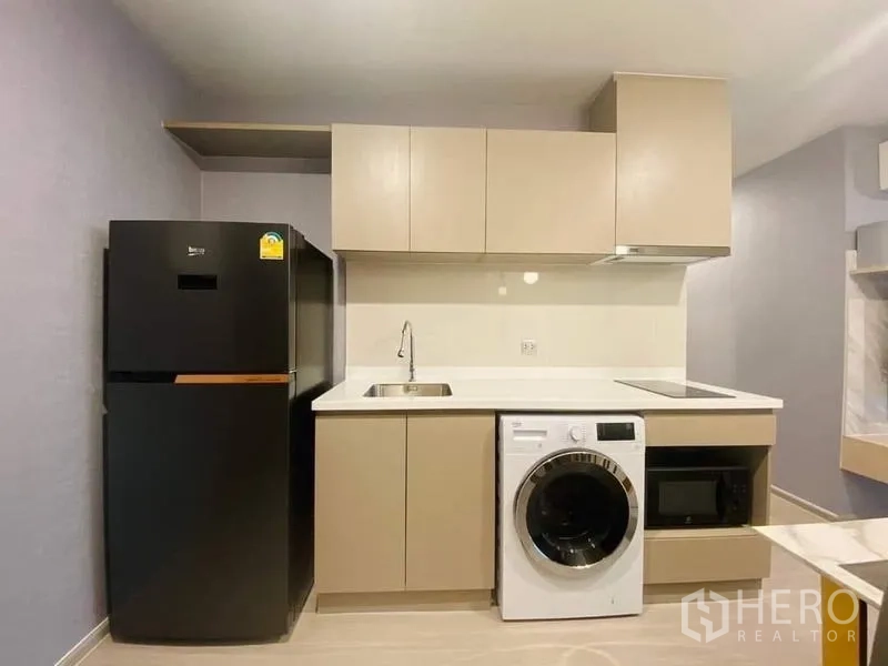 คอนโด ให้เช่า - ครัวกะทัดรัด ตู้ลอยสีเบจ ตู้เย็นสีดำ เครื่องซักผ้า เตาไฟฟ้า และไมโครเวฟ