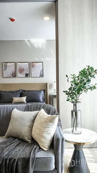 Condominium for sale in Khlong Toei, Bangkok - Detail of sofa and side table with indoor plant, with the bedroom and artwork in the background.