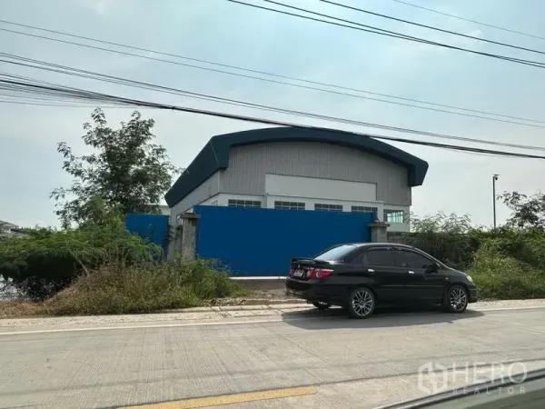 工厂 出租在Pak Kret, Nonthaburi - 临街工厂外观，蓝色围墙与弧形金属屋顶，靠混凝土道路。